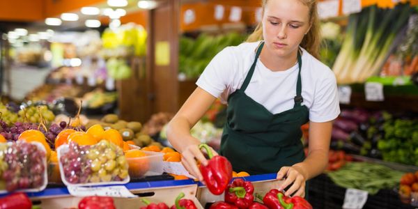A woman arranging red bell peppers at a market stall.