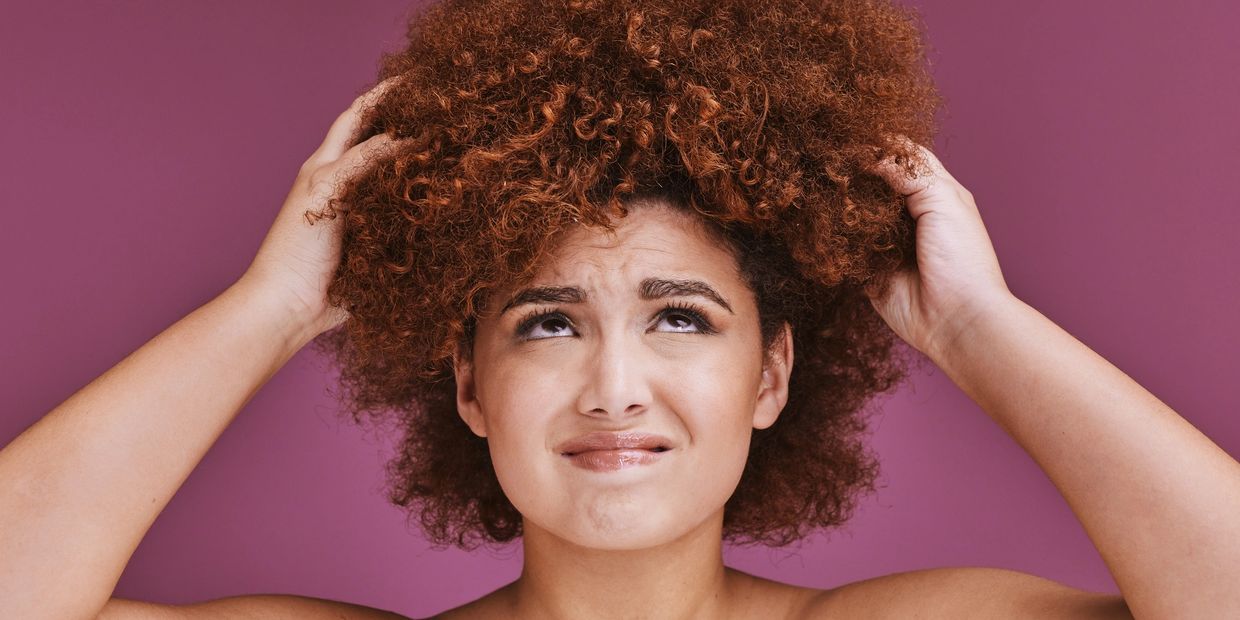 Woman with curly hair looks frustrated while holding her head.