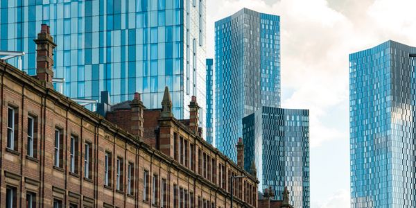Modern glass skyscrapers rise behind historic brick buildings in a cityscape.