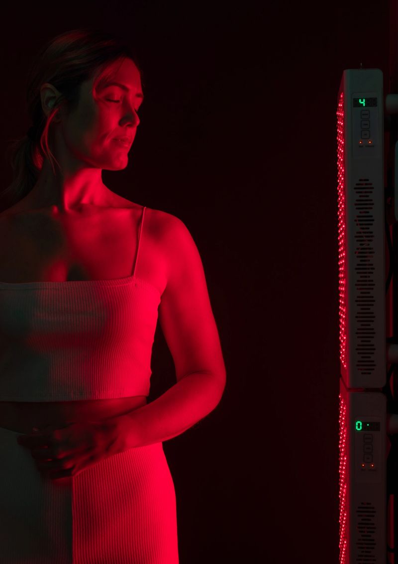 Woman getting red light therapy in a beauty spa. Mature woman standing next to a red light device. Anti-aging and skin care treatment.