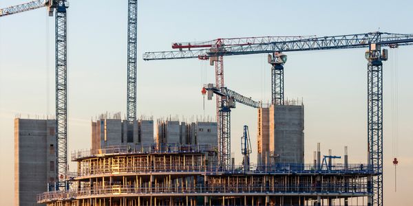 Multiple cranes working on a high-rise building construction site at sunset.