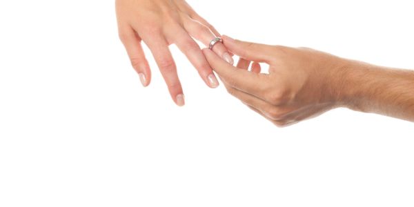 Hand placing a ring on another person's finger against a white background.