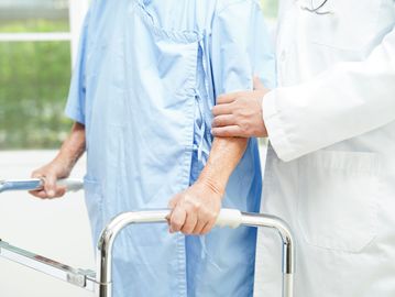 Doctor supporting elderly patient using a walker.
