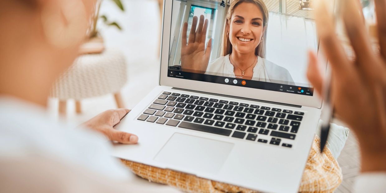 Woman video calling on laptop, smiling and waving.