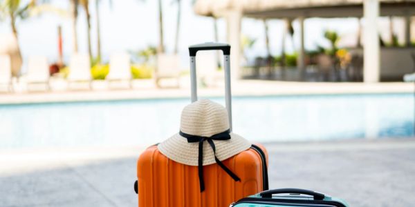Two suitcases by a pool with a hat on one.