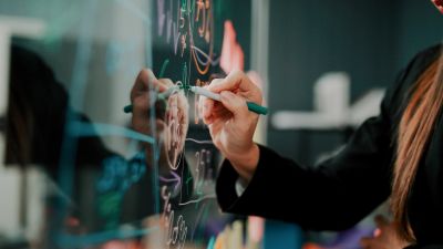 Person writing complex formulas on a glass board.