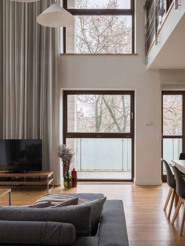 Modern living room with large windows, gray sofa, and wooden flooring.