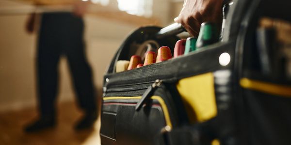 Close-up of a hand carrying a tool bag filled with screwdrivers.