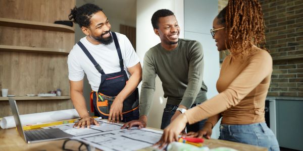 Three people discussing architectural plans around a table in a modern workspace.