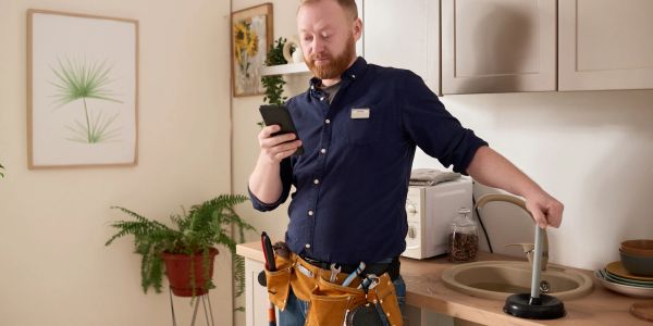 Plumber using phone while holding a plunger.