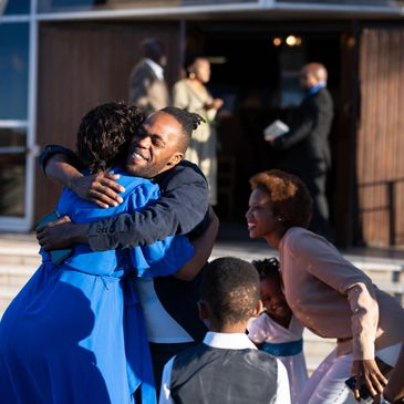 People warmly embracing and greeting each other outdoors.