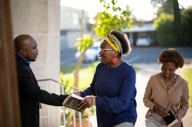 Paster greets & welcomes a senior woman on the steps  as she arrives to the church service