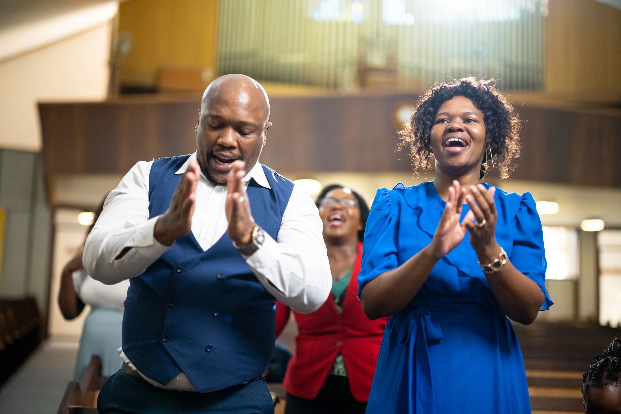 Two people clapping and singing joyfully indoors.