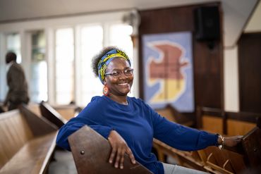 Smiling woman sitting in a church pew wearing a blue shirt and colorful headband.