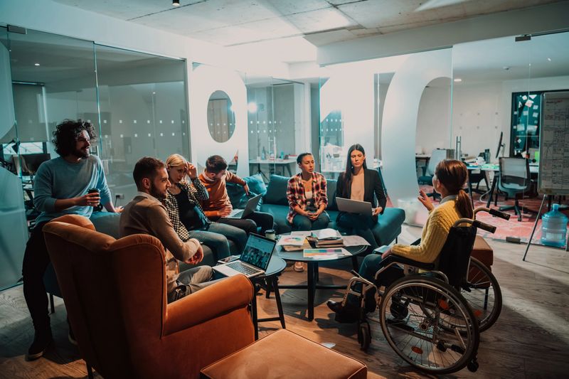 A businesswoman in a wheelchair having a business meeting with the team at a modern office. A group of young freelancers agree on new online business projects.