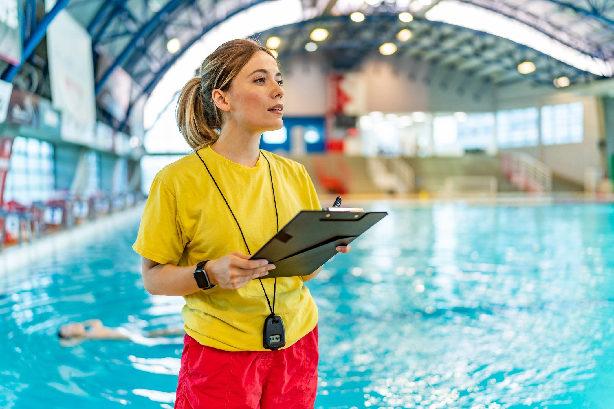 Lifeguard standing by the pool with clipboard.