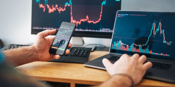 Person analyzing stock charts on multiple devices.