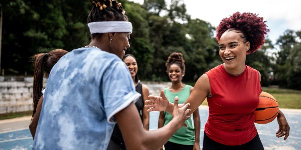 Women playing basketball and sharing a high-five on an outdoor court.