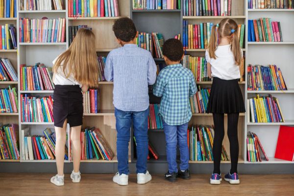 Four children looking at bookshelves in a library.