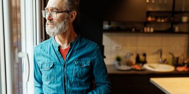 Older man with glasses looking thoughtfully out a window.