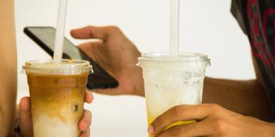 Two hands holding iced coffee drinks with straws.