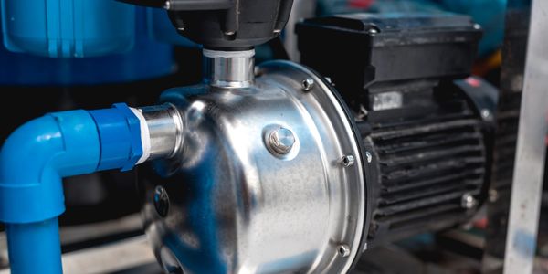 Close-up of a metallic water pump connected to blue pipes.