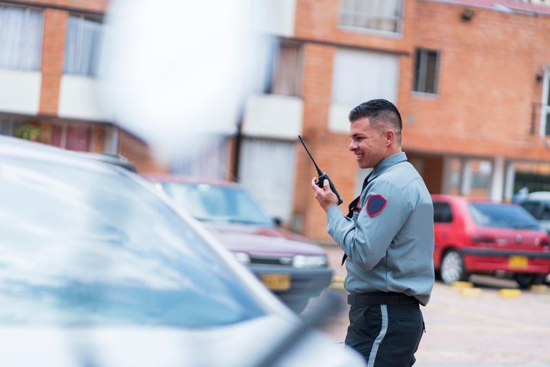 Average age Latino man in his 30s dressed in a security guard uniform is inside the building he works for taking bills for vehicles parked in the parking lot