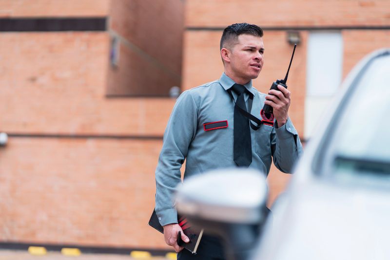Average age Latino man in his 30s dressed in a security guard uniform is inside the building he works for taking bills for vehicles parked in the parking lot