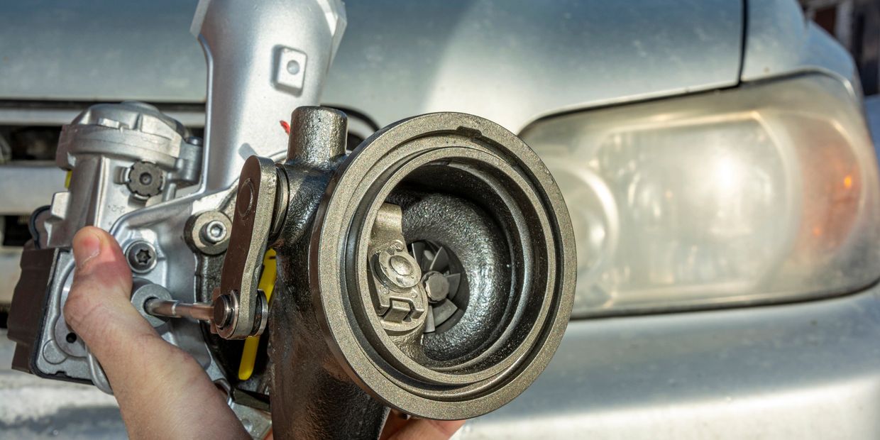 Hand holding a turbocharger in front of a car's headlight.