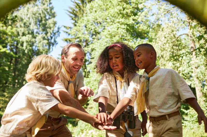 Diverse group of scouts stacking hands and huddling while exploring nature together in forest