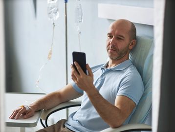 Man receiving IV therapy while using a smartphone in a medical setting.