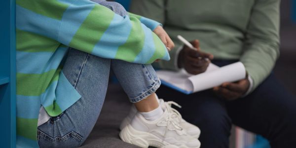 A person sitting with knees up talking to a counselor taking notes.