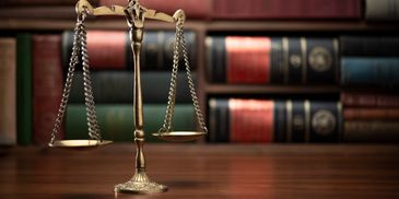 A brass balance scale on a wooden table with blurred law books in the background.