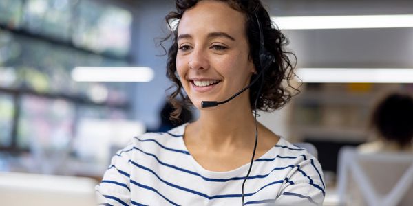 Woman with headset smiling while working in a bright office.