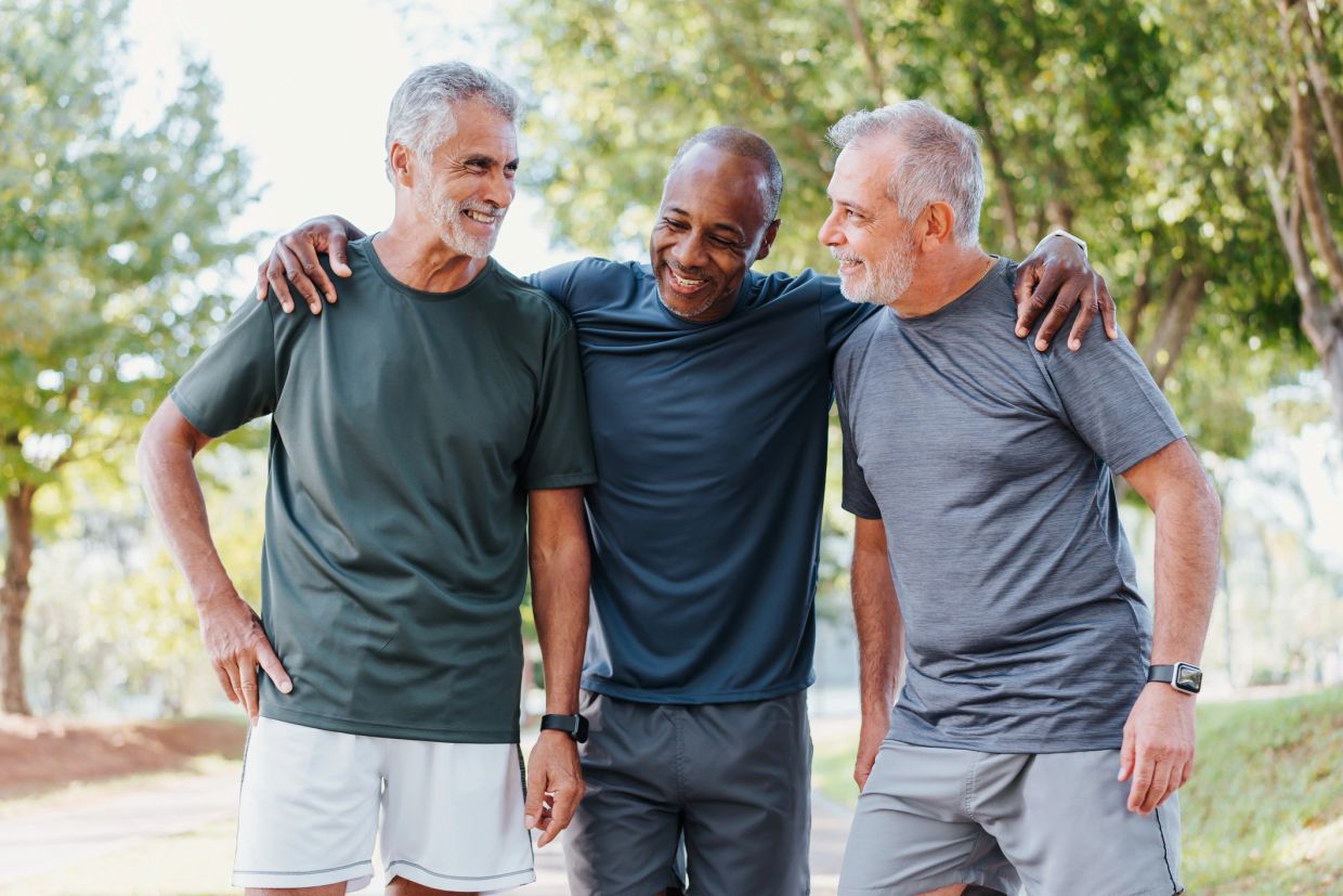 Three older men smiling outdoors, arms around each other.