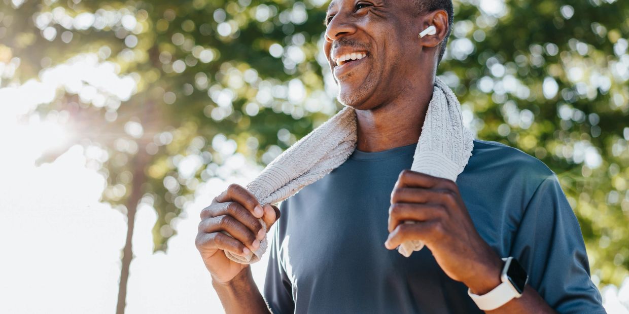 Smiling man with towel and earbuds after workout outdoors.