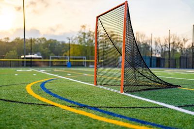 A lacrosse goalpost on a sports field at sunset.