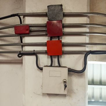 Electrical conduit pipes connected to colored junction boxes on a wall.