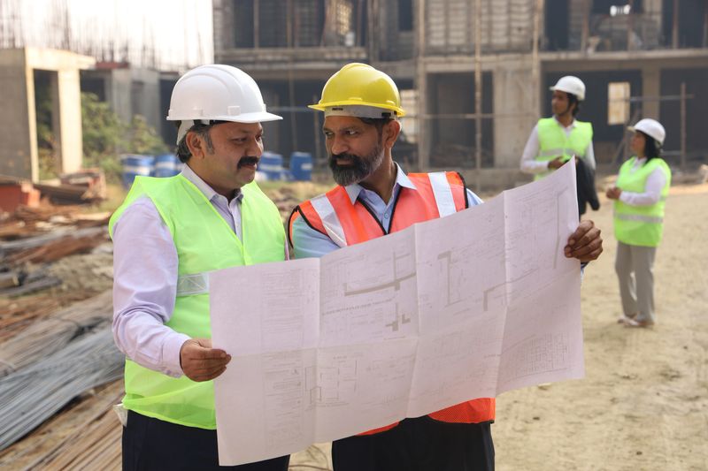 Construction engineer working on a construction site reviewing and analysing the work in progress. Manager Holding blueprint in hand to examine or inspect the work flow and the quality of the work.