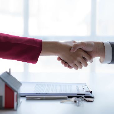 Apretón de manos sobre contrato con llaves y casa en miniatura.
