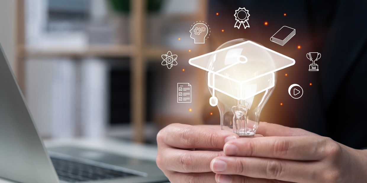 Hands holding a glowing light bulb with education icons and a graduation cap graphic.