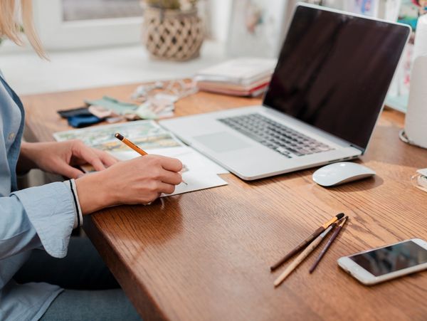 Person writing on paper at a wooden desk.