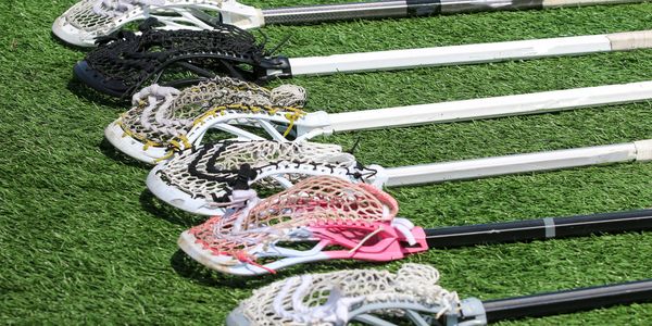 A row of lacrosse sticks laid out on grass.