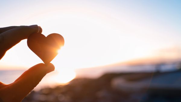 Hand holding heart shape against sunset.