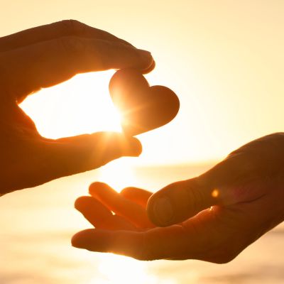 Hand passing a heart-shaped object at sunset.