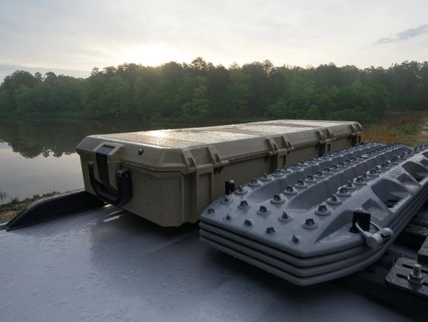 Military equipment on a vehicle roof near a lake at sunrise.
