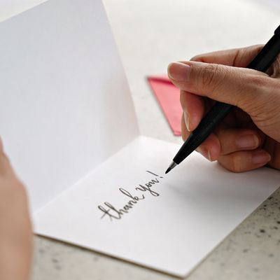One hand holding a thank you card while the other hand is holding a pen.