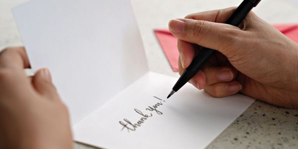 Person writing 'thank you!' in a card.