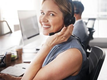 Smiling customer service representative wearing a headset in an office.