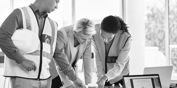 Three professionals collaborate over blueprints in an office.